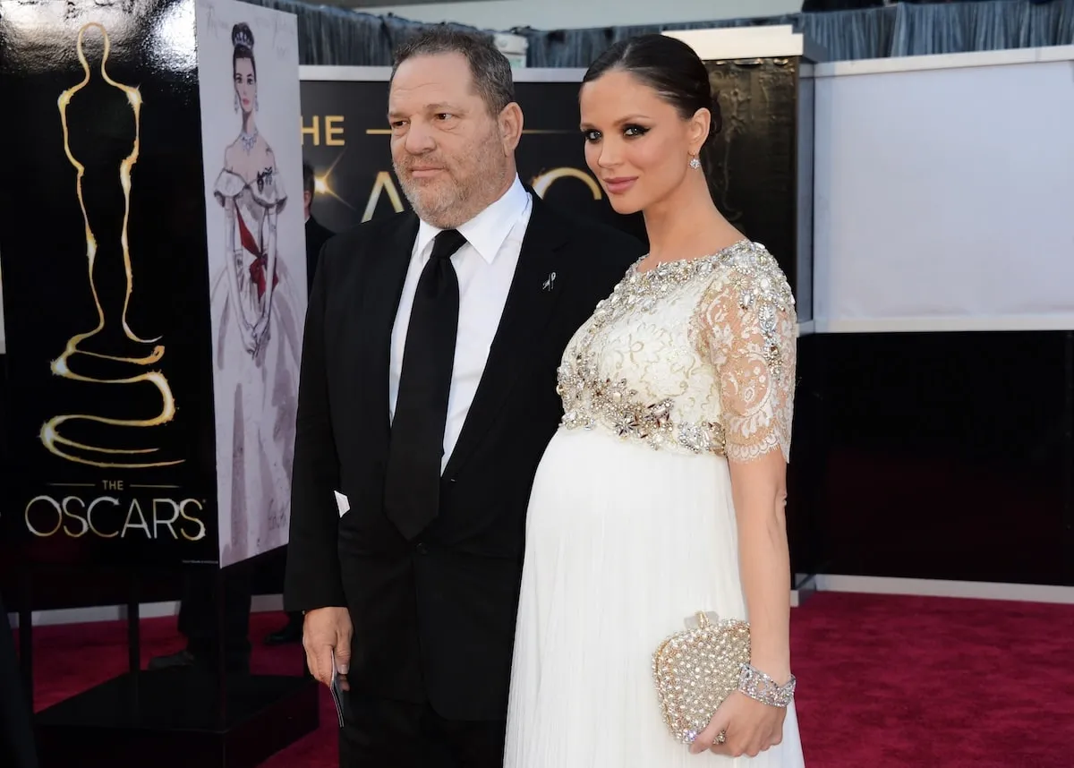 Wearing a tuxedo and a white gown respectively, Harvey Weinstein and Georgina Chapman smile on the red carpet at the 2013 Oscars
